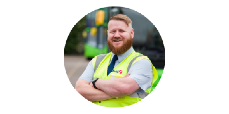 Photo of man with ginger hair standing in front of bus wearing a yellow high viz jacket. David