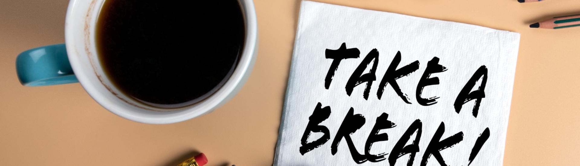 Coffee, pens, biscuits on desk with a note saying 'Take a break!'