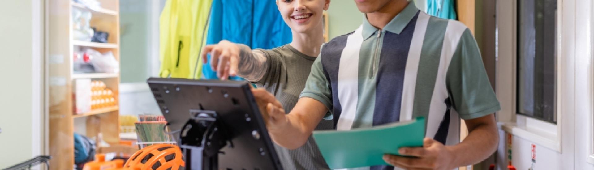 Young male apprentice being shown how to use digital till system in bike shop
