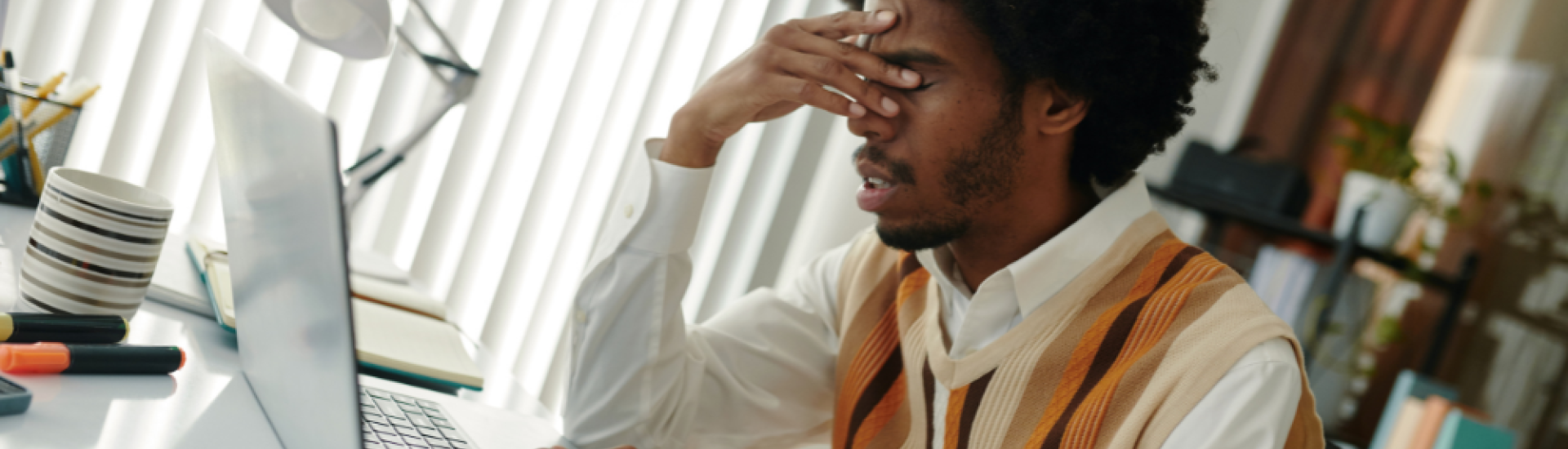 A person sat in from of a laptop with hand partially covering his face and looking stressed