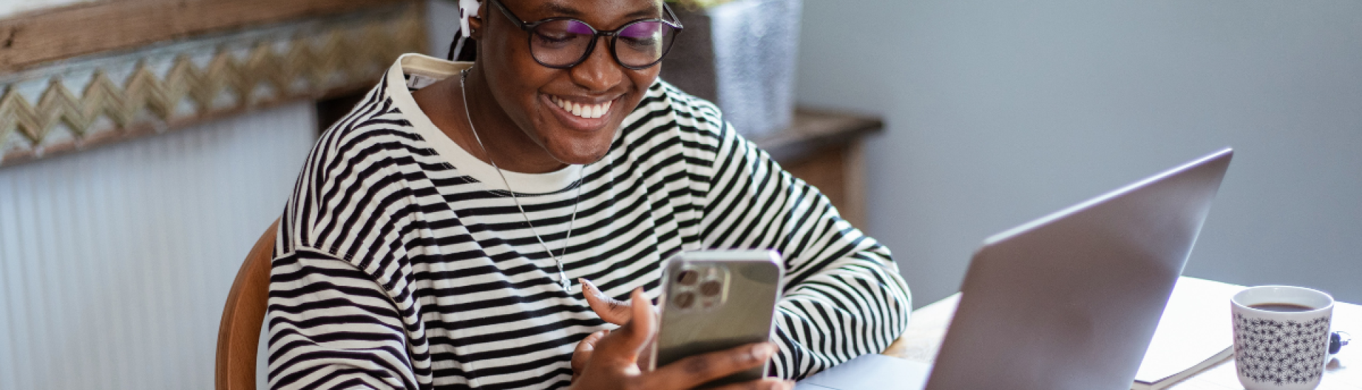 An employee sat at a desk, smiling and looking at her phone with a cup of tea