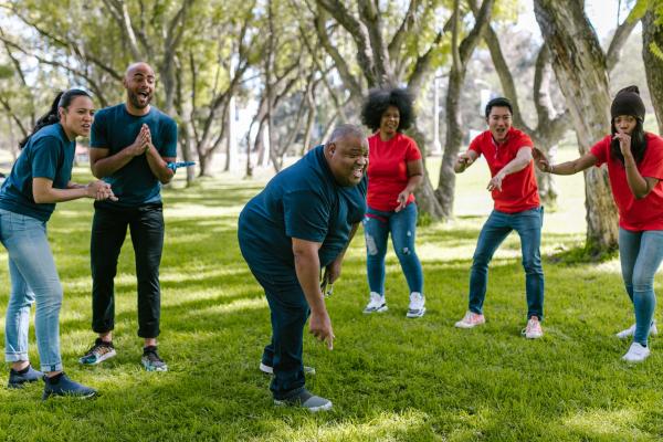 Group of six people wearing blue and red tshirts playing a game with a man in the centre throwing a ball