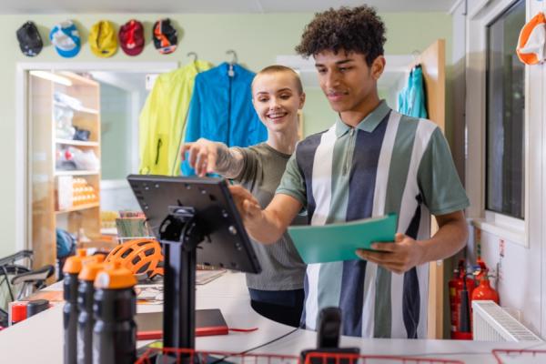 Young male apprentice being shown how to use digital till system in bike shop