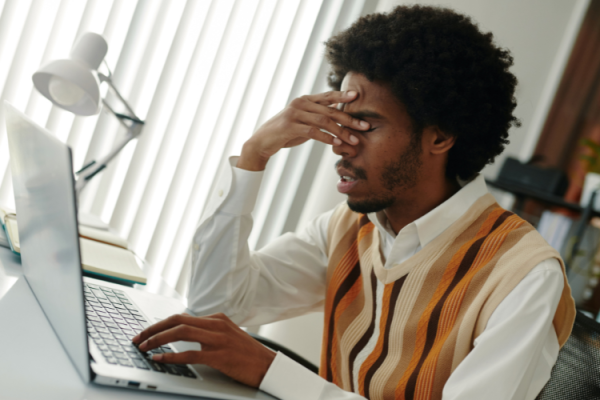 A person sat in from of a laptop with hand partially covering his face and looking stressed