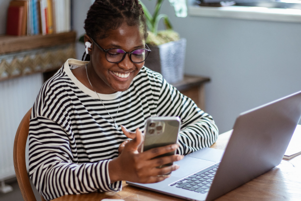 An employee sat at a desk, smiling and looking at her phone with a cup of tea